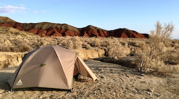 Camping tent overlooking red and brown Aktau Mountains in Altyn Emel