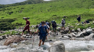 Hikers crossing a fast-flowing rocky mountain stream with trekking poles during a multi-day trek near Almaty, Kazakhstan