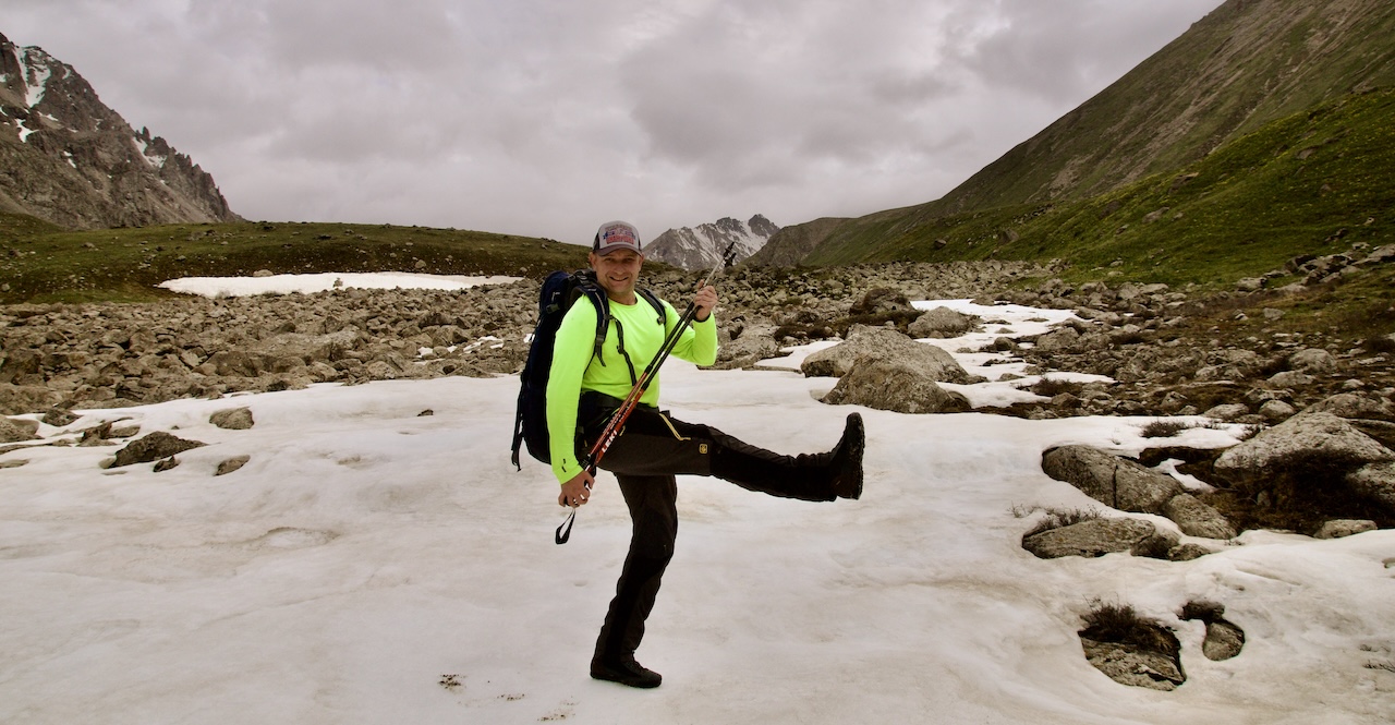 Mountain guide with trekking poles standing on a patch of snow in the Northern Tien Shan during a three-day trek from Big Almaty Lake across Almaty-Alagir Pass to Prokhodnoye Gorge