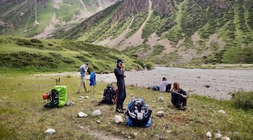 Trekkers resting beside a mountain river in a green valley of the Northern Tien Shan