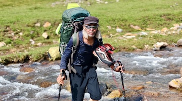 Mountain guide crossing a shallow mountain stream with trekking poles