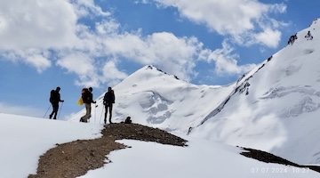 Three trekkers standing on a snowy mountain ridge surrounded by glaciers
