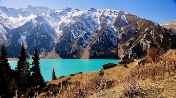 Turquoise Big Almaty Lake surrounded by autumn mountain slopes and Tien Shan spruce trees