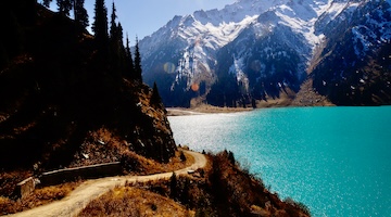 Paved mountain road winding above the turquoise waters of Big Almaty Lake